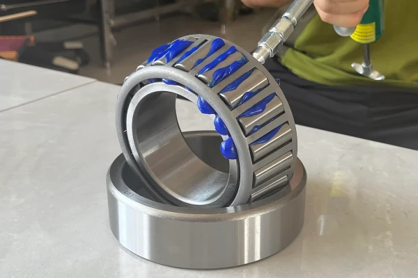 An image showing the process of applying grease to a tapered roller bearing, highlighting the importance of lubrication.