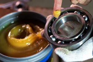 Close-up of a mechanic applying grease to an industrial rolling bearing to ensure smooth rotation.