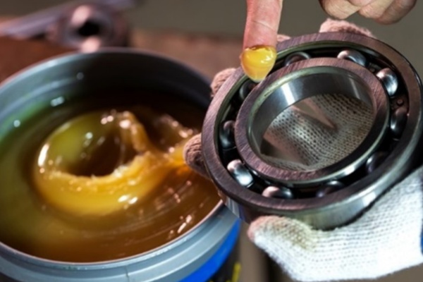 Close-up of a mechanic applying grease to an industrial rolling bearing to ensure smooth rotation.