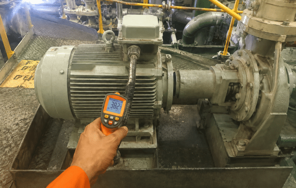 Technician checking bearing housing temperature on an industrial motor and pump with an infrared thermometer